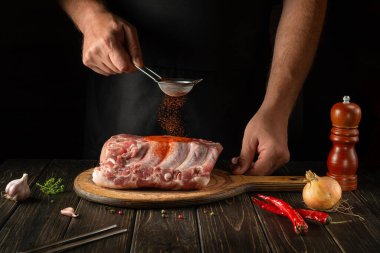 Close-up of a chef sprinkling paprika on fresh meat ribs. The concept of cooking delicious street food or grill. Black background with space for advertising.