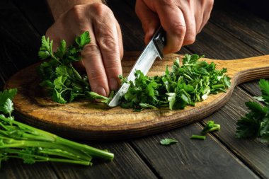 The chef cuts green parsley on a cutting board with a knife for preparing a vegetarian dish. Peasant food