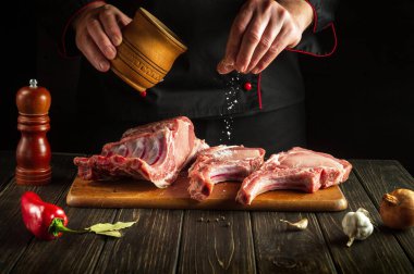 Aşçı çiğ kaburgalara tuz serper. Otel için lezzetli yemekler pişirme fikri.
