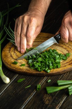 Thecook cuts green onion on a cutting board with a knife for preparing a vegetarian dish
