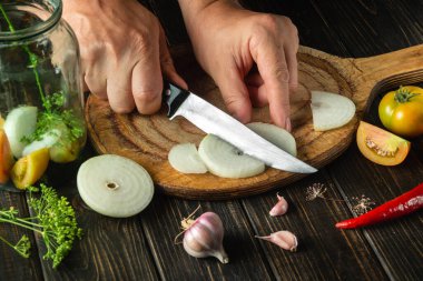 Preservation of tomatoes in a jar for the winter. The chef cuts the onion with a knife on the kitchen cutting board. Peasant food.