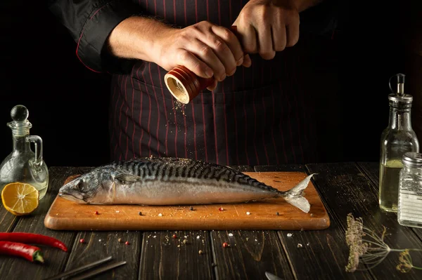 The fish chef adds pepper to fresh mackerel before preparing a delicious meal in the hotel kitchen.