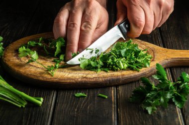 Cook cuts green parsley on a cutting board with a knife for cooking vegetarian food.