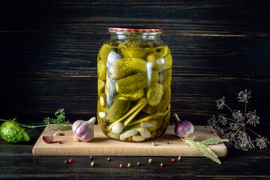 Jar with canned cucumbers and spices on a wooden board after cooking. Place for an inscription or advertising.