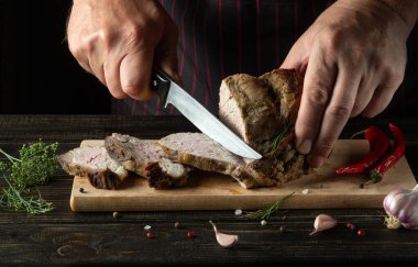 Professional chef slicing grilled beef meat on a cutting board. Work environment on the kitchen table with condiments or spices. Black or dark background with space for hotel menu.