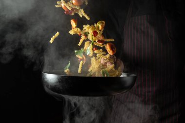 Cook throws food on a hot pan. Thai street food pasta with spices and vegetables. Space for advertising on a dark background