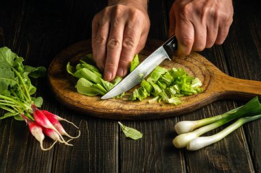 The chef cooking a salad in the kitchen. Close-up of the hands of the cook with a knife cuts the leaves