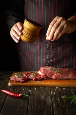An experienced chef salts raw fresh beef before roasting or barbecuing. Working environment in the kitchen of a restaurant or hotel
