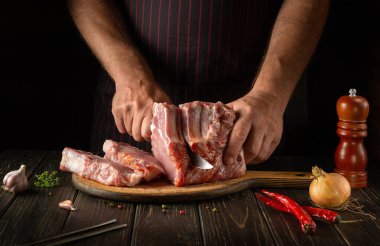 The chef or butcher cuts raw ribs on a cutting board before grilling. Meat dish idea for a hotel or restaurant
