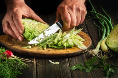 The hands of the cook with a knife cut fresh raw cabbage on a cutting board for cooking vegetable food