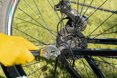 A mechanic repairs a bike on the street with a wrench. Close-up of a master hand in a glove.