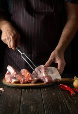 Cooking raw meat ribs by the chef hands in the restaurant kitchen. The cook hand is holding a fork. Delicious grilled lunch.