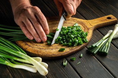 The chef slicing green onions on a cutting board with a knife for cooking vegetarian food.