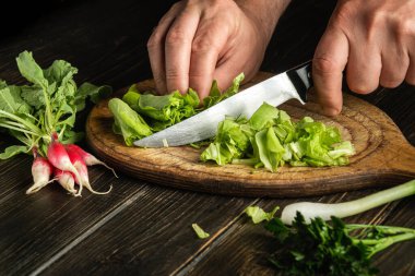 The chef cooks a salad of fresh vegetables. Cutting green leaves with a knife on a cutting board