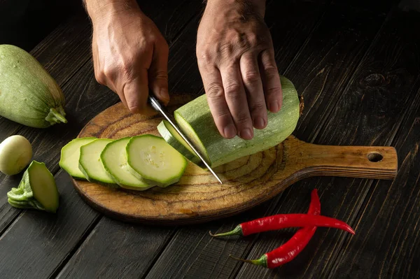 Slicing zucchini with a knife before cooking by chef\'s hands on a wooden cutting board. The thick flesh of a vegetable marrow is used in the UK