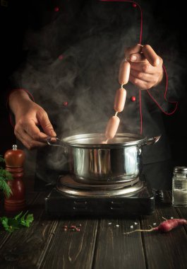 Profesyonel şef sosisleri kaynayan bir kaba koyar. Lezzetli bir kahvaltı ya da akşam yemeği hazırlıyorum.