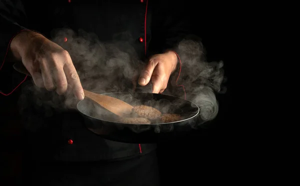 Professional cook frying burger cutlets in a frying pan. Close-up of a chef hands with a hot pan in the kitchen. Free space for advertising