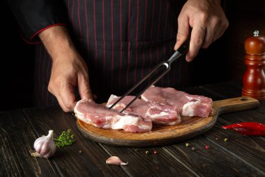 Cooking raw meat ribs by the chef hands in the restaurant kitchen. The cook hand is holding a fork. Delicious grilled lunch.