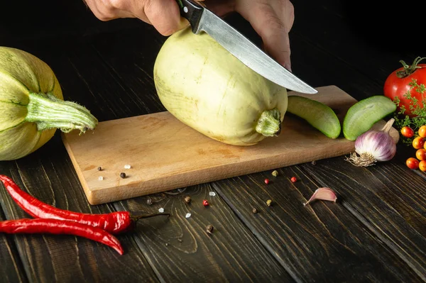Slicing zucchini with a knife before cooking by chef's hands on a wooden cutting board. The thick flesh of a vegetable marrow is used in the UK