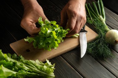 Şef mutfağın kesim tahtasında salata pişirir. Diyet yemek hazırlarken ellerinizi masaya koyun.