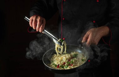 Şef sıcak tavada baharatlı ve baharatlı lezzetli spagetti pişirir. Karanlık arka planda reklam için yer var. Restoran veya otel menüsü
