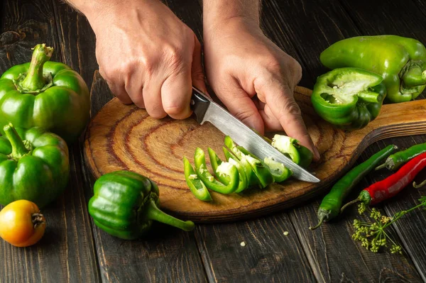 The chef cuts green pepper on a cutting board for making spicy adjika. Peasant delicious food.