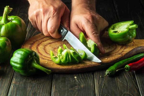 The cook cuts green peppers on a cutting board for cooking lecho. Peasant delicious food.