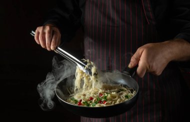 Bir şefin elleriyle baharatlı ve baharatlı spagetti pişirmek. Siyah arkaplanda otel tarifi veya menüsü.
