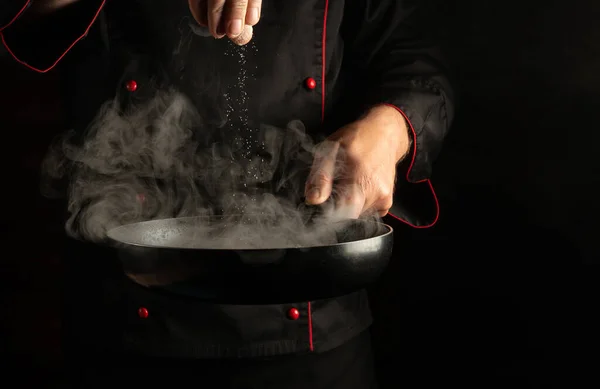 The cook adds salt to meat steaks in a hot pan with steam. Cooking meat patties for a burger