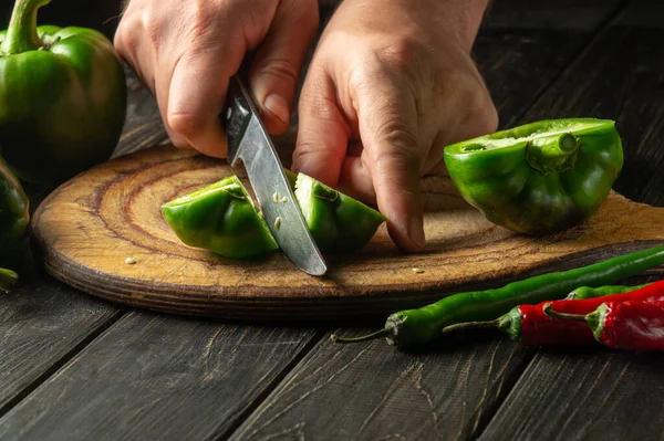 The chef cuts fresh green peppers to prepare a delicious salad at home. Peasant food.