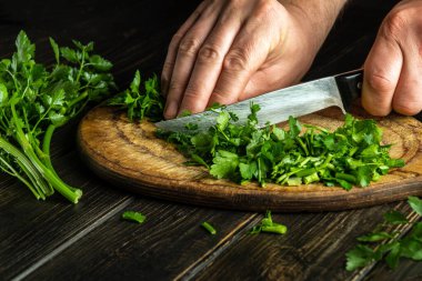 Profesyonel şef vejetaryen yemeği hazırlamak için kesme tahtasıyla yeşil maydanoz kesiyor.