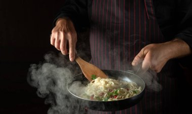 Aşçı, haşlanmış tavada baharat ve baharatla lezzetli bir spagetti hazırlıyor. Karanlık arka planda reklam için yer var. Restoran veya otel menüsü