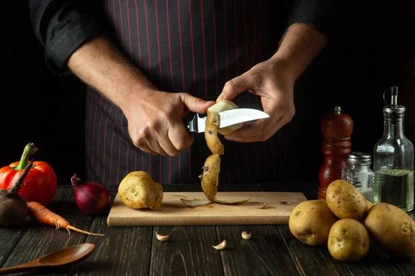 The chef peels potatoes for cooking French fries. Working environment in the kitchen of a restaurant or cafe.