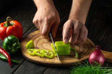 Lezzetli bir yemek hazırlamak için kesme tahtasındaki yeşil biberleri şefin elleriyle dilimlemek. Vejetaryen menüsü ya da tarif fikri