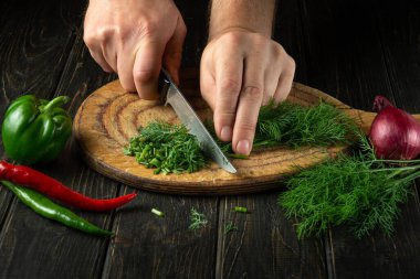 Aşçı kesme tahtasındaki yeşil taze dereotu bıçakla keser. Restoran veya otel için vejetaryen menüsü.