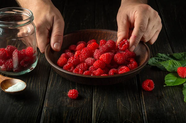 The chef prepares a sweet drink or fresh raspberry compote. Concept on dark background with space.