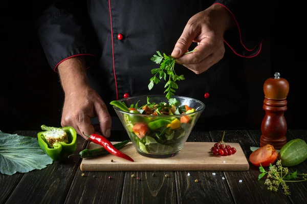 Delicious vegetable salad by the hands of the chef. The concept of a menu or recipe for a hotel on a dark background