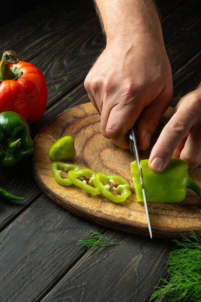 Close-up of the chef hands with a knife cut fresh pepper on the cutting board of the restaurant kitchen.