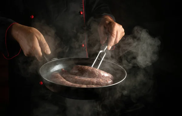 Professional chef flips the meat sausage in a hot pan with a fork. Preparing a delicious meal in the kitchen