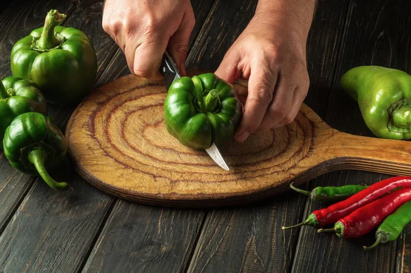 The cook cuts fresh green peppers to prepare a delicious salad at home. Peasant food