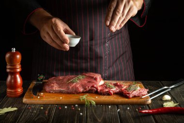 Şef kızarmadan ya da ızgara yapmadan önce çiğ et tuzlar. Restoranın ya da otelin mutfağında çalışma ortamı