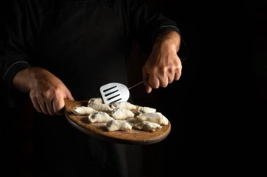 Kesme tahtasında çiğ et pelmeni. Mutfakta şefin ellerinden hamur tatlısı pişiriyorum. Siyah arka planda lezzetli bir öğle yemeği ya da kahvaltı
