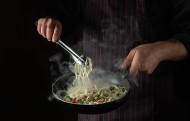 Bir aşçının elleriyle tavada spagetti pişirmek. Siyah arka planda otel tarifi ya da menüsü. Sebze ve baharatlı lezzetli makarna..