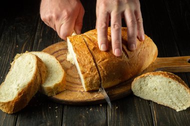 Tam tahıllı ekmek mutfak tahtasına konmuş ve şefin elinde bıçak var. Masanın üzerinde taze ekmek var. Mutfak masasında buğday ekmeği mi yoksa sağlıklı beslenme ve geleneksel fırın konsepti mi?.