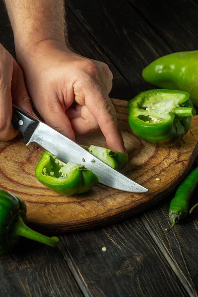 The chef cuts green peppers on a cutting board for cooking lecho. Peasant delicious food.