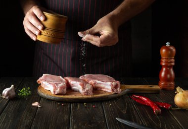 Aşçı akşam yemeğini hazırlamadan önce mutfağın kesme tahtasındaki çiğ et bifteklerini tuzlar. Lezzetli ızgara fikri..