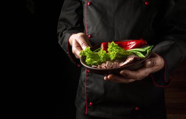 Profesyonel şef yemeğini dilimlenmiş biftek ve sebze tabağında sunar. Siyah arkaplanda otel menüsü veya tarifi için boşluk