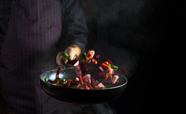 Bir aşçının elinden kızartma tavasında sebze pişirmek. Gıda konsepti siyah arka planda. Sebze menüsü veya otel tarifi