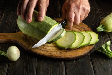 Lezzetli bir yemek hazırlamadan önce ahşap kesme tahtasıyla kabak kesen bir aşçının yakın çekim elleri.