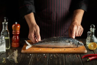 Şef otel mutfağında uskumru ya da Scomber hazırlar. Koyu bir arka planda balık pişirme kavramı